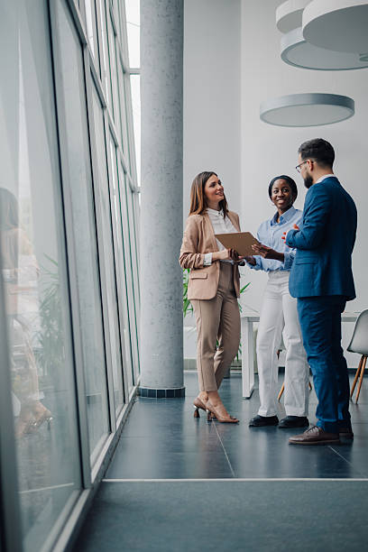 business colleagues reviewing documents and discussing work in office hallway
